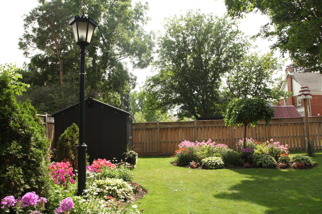 Wide-angle photo of a backyard setting showing a finished garden shed in grey with black trim, located on a manicured lawn beside a wooden fence